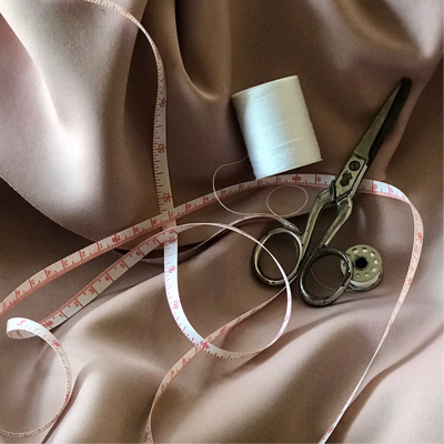 measuring tape, scissors, and roll of thread yarn laying ontop of cream colored fabric